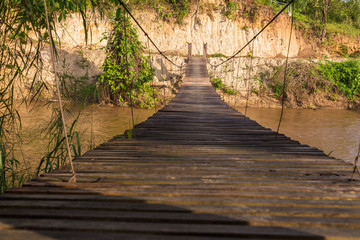 Fototapeta na wymiar Old wooden sling brige hanging above river in northern Thailand