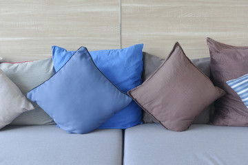 Blue and brown pillows lay on light blue sofa with wooden wall in background.