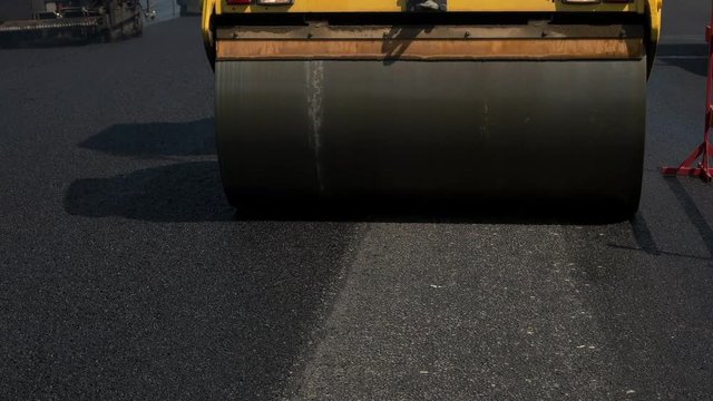 Steel wheel of road roller. Black asphalt under sunlight. Planned repair of roadway. Pressure and temperature.