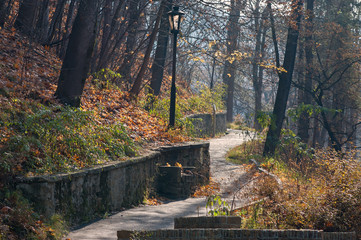 Old lantern standing at terrenkur. The path going up the hill through autumn forest with slopes full of fallen leaves, Kislovodsk