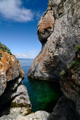 Clear emerald water in a small bay surrounded by strange shape cliffs. On the rocks growing moss and lichen. Summer, Lake Baikal, Olkhon Island