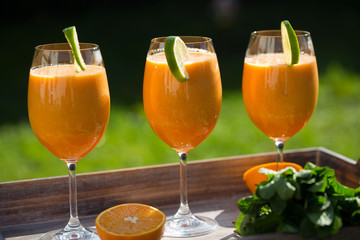 Smoothie mit Melone, Orange, Karotte, Limette - Frische Früchte, auf Tablette im Garten