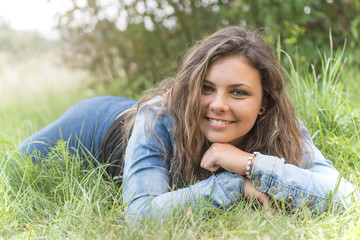 Smiling long hair teenage girl is lying in the grass. Girl is looking at the camera.