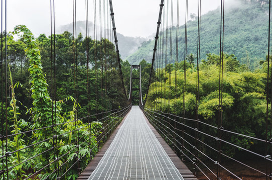 Fototapeta Steel suspension bridge, crossing the river in the woods