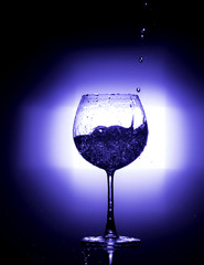 Pouring water into wine glass with black background blue white balnce