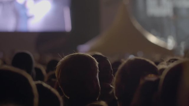 View From Behind Of Some Cheering Fans At A Life Concert, Hands Up And Applauding People In Dark