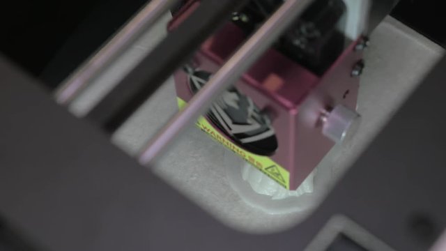 Top close-up view of mechanism of 3d printer in process. It makes object with white plastic