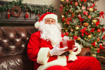Fototapeta na wymiar Santa Claus with giftbox on background of sparkling firtree. Christmas