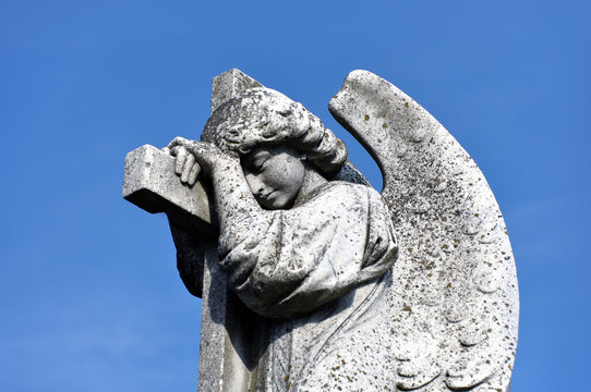 Ancient sculpture of a crying angel of concrete against the blue sky.