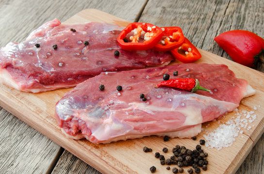 Raw duck meat on a cutting board with pepper and salt. Cooking meat