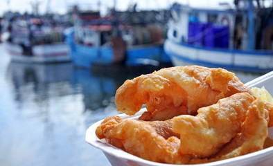 Battered fish served on a plate against fishing boats at sunset