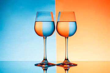 Two wineglasses with water over blue and orange background.