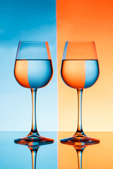 Two wineglasses with water over blue and orange background.