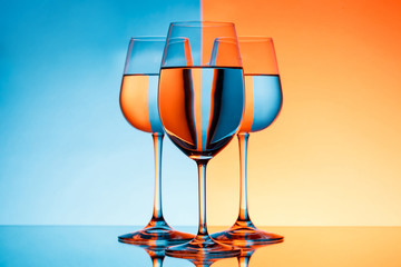 Three wineglasses with water over blue and orange background.