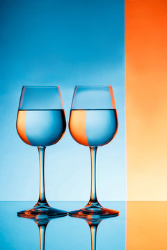 Two wineglasses with water over blue and orange background.