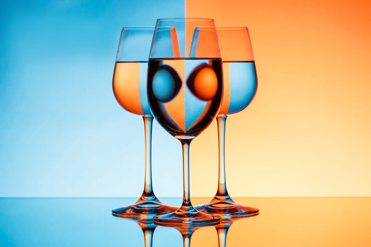 Three wineglasses with water over blue and orange background.