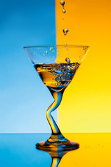 Water pouring in glass over blue and yellow background.