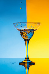 Water pouring in glass over blue and yellow background.