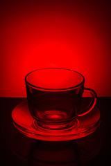 Glass transparent empty mug of tea and saucer on a red backgroun