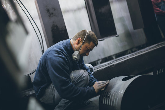 Metallurgy industry. Factory for production of heavy pellet stoves and boilers. Manual worker painter on his job. Extremely dark conditions and visible noise.