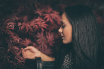 Sinnliches Frauengesicht vor roten Blättern - Rassige Frau im Seitenprofil schaut verträumt 