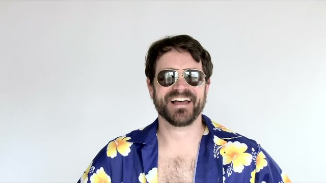 Model released man in studio puts on sunglasses and wears hawaiian shirt as if he is on vacation.