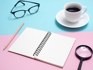 Top view of colorful cup of coffee , notebook , glasses on blue and pink  background 