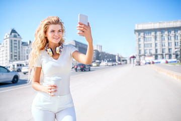 Coffee and me / Beautiful young woman with music headphones and a take away coffee cup, taking picture of herself, selfie against urban city background.