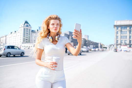 Coffee and duck face / Beautiful young woman with music headphones and a take away coffee cup, taking selfie and making duck face against urban city background.