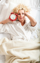 beautiful woman in a white robe with an alarm clock in hands