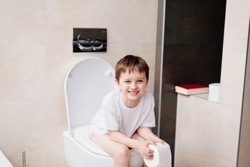 Little 7 years old boy sitting on toilet. - obrazy, fototapety, plakaty