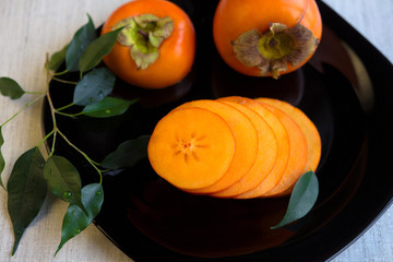Cut a ripe persimmon on black plate
