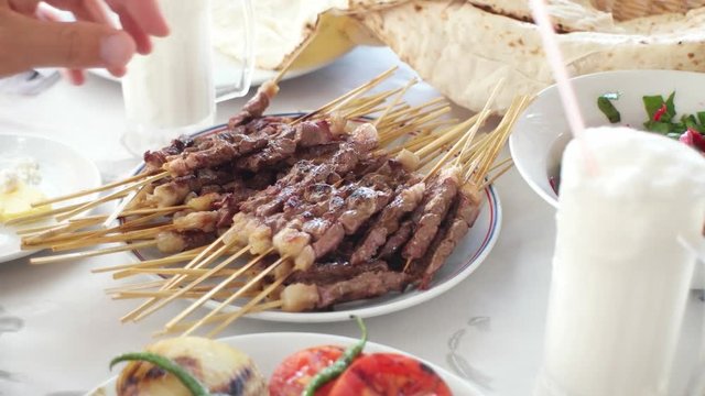 Hot roasted meat shish kebab with skewer on plate and traditional Turkish drink Ayran. Customers taking kebabs with hands at restaurant