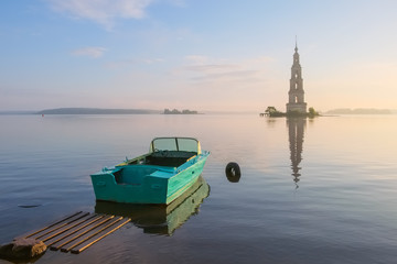 Fototapeta na wymiar Landscape with flooded bell tower of the Cathedral of St. Nicholas in the town of Kalyazin on the Volga River in the early summer morning at sunrise with a motor boat on the shore