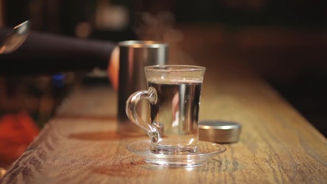 Footage of a woman placing a glass of hot water on a counter, in a bar.
