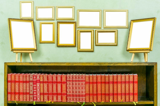 Many empty golden wooden frames with copy space on green wallpapered wall. Bookshelf with red books.