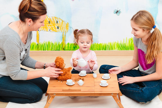 Little girl playing with mom and sister at tea party using child