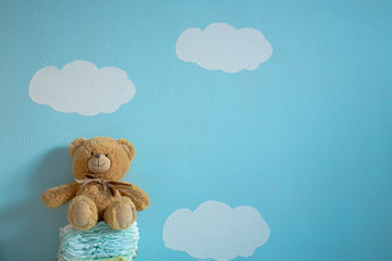 The toy is sitting on the diapers in the wall background of blue sky and clouds