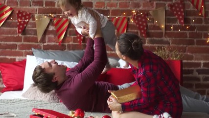 Christmas morning.Young family gleefully congratulates each other Marry Christmas.On bed there are many Christmas gifts in bright packings and Christmas-tree decorations.Merry Christmas.Happy New Year