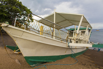 White passenger boat on a beach sand. Small catamaran parked on a seashore.