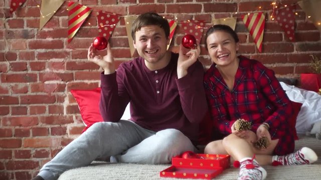 Christmas morning. Young couple sitting on the bed. Man and woman are in a good mood. They fool around. Christmas Holidays is the perfect time to relax and chat. Merry Christmas and a Happy New Year.