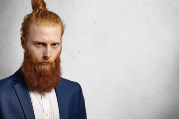 Serious successful redhead Caucasian entrepreneur with bun hairstyle and fuzzy beard dressed in...