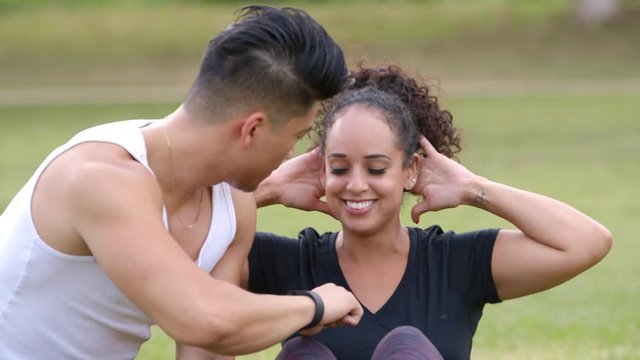 In a  park a young man times his workout buddy while she does her sit-ups.