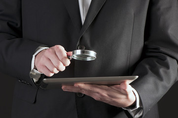 Businessman holding magnifying glass and digital tablet