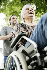 Sohn schiebt seine demenzkranke Mutter, Seniorin,  im Rollstuhl