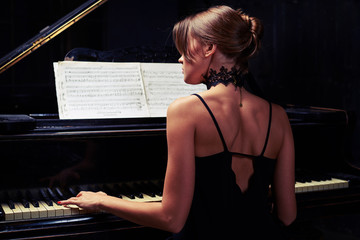 Young woman sitting down to the piano in black back naked dress