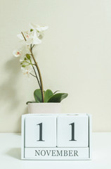 Closeup white wooden calendar with black 11 november word with white orchid flower on white wood...