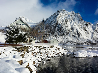 Snowy peaks and typical house of fishermen are refelcted in the frozen sea surrounded by snow Lofoten Islands Norway