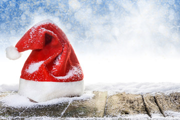 Weihnachtsmütze auf verschneitem Holzboden vor blauem Hintergrund mit Bokeh