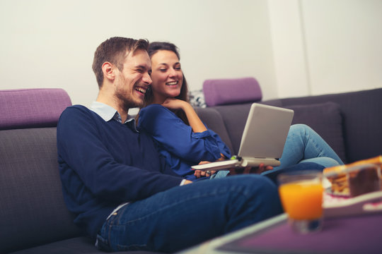 Happy young couple using a laptop at home and smiling